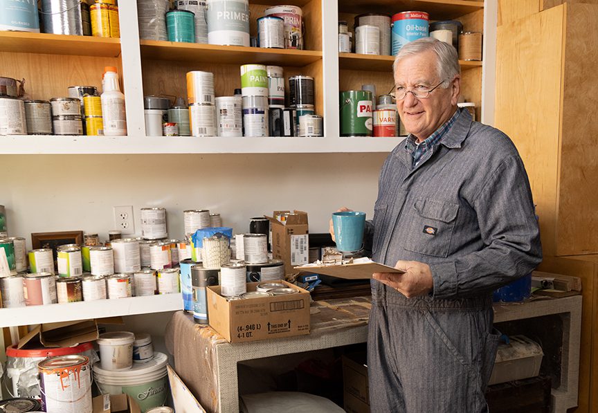 man holding clipboard in front of shelf of canned paints